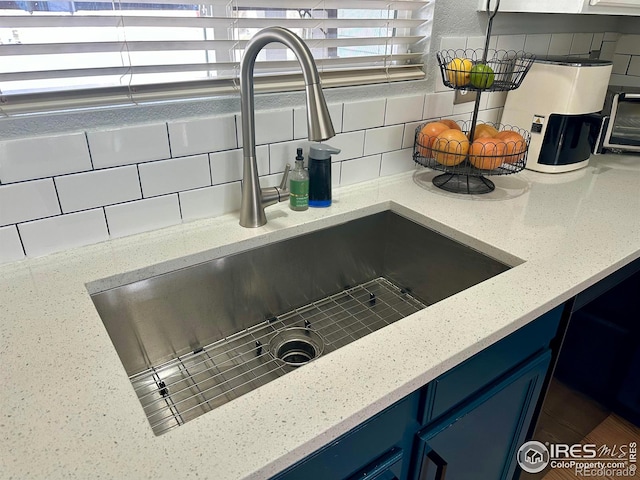 interior details with blue cabinets, light stone countertops, sink, and decorative backsplash