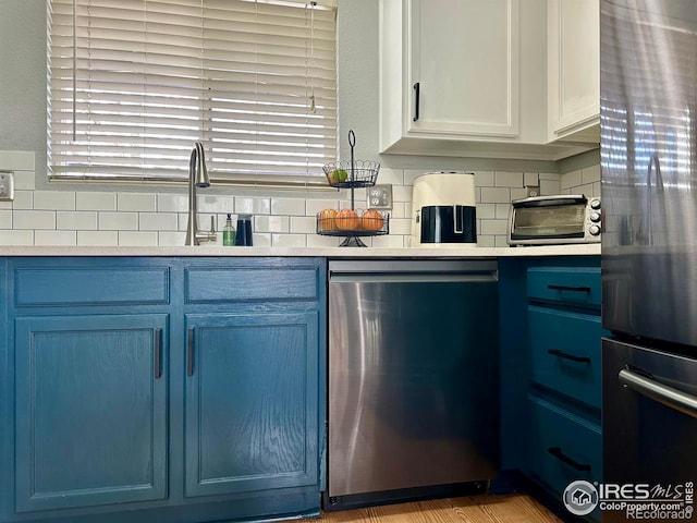 kitchen featuring white cabinetry, backsplash, fridge, stainless steel dishwasher, and blue cabinetry