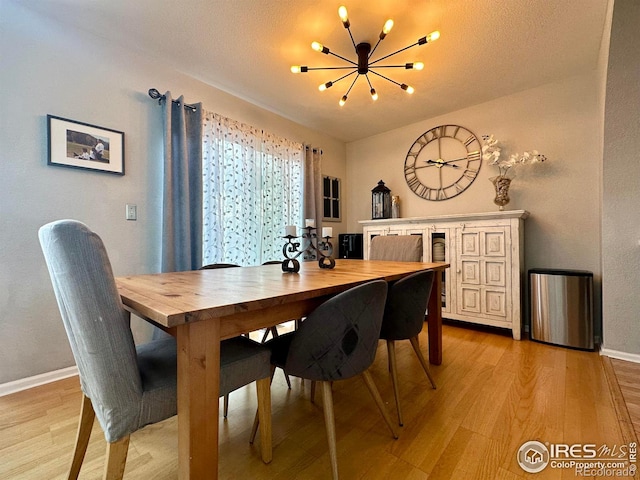 dining room featuring a notable chandelier, vaulted ceiling, and light wood-type flooring