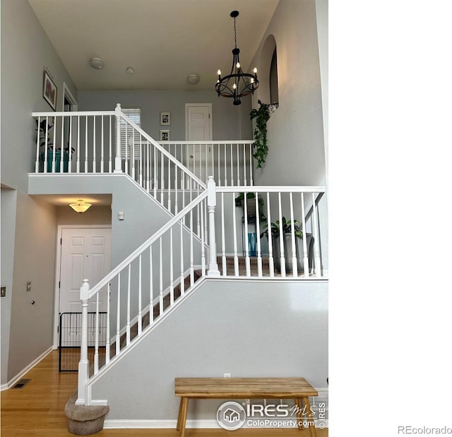 stairway featuring hardwood / wood-style floors, a towering ceiling, and a notable chandelier