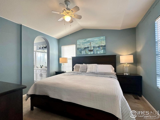 bedroom with ceiling fan, ensuite bath, carpet flooring, and vaulted ceiling