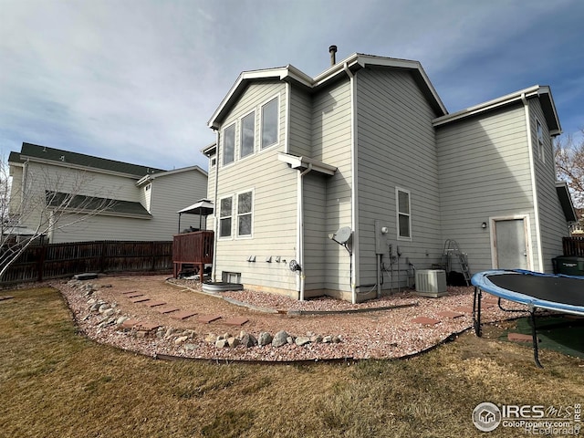 rear view of house featuring a trampoline, a yard, and central AC