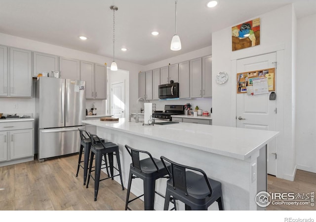 kitchen featuring stainless steel appliances, gray cabinets, an island with sink, and hanging light fixtures