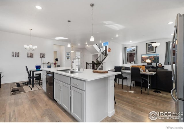 kitchen featuring sink, wood-type flooring, hanging light fixtures, stainless steel appliances, and a kitchen island with sink