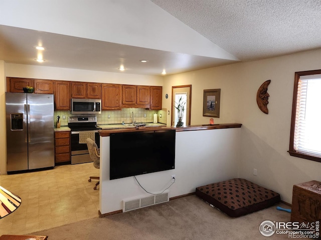 kitchen with lofted ceiling, sink, appliances with stainless steel finishes, kitchen peninsula, and backsplash