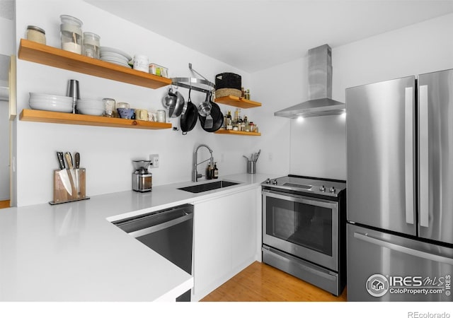 kitchen with sink, light hardwood / wood-style floors, kitchen peninsula, stainless steel appliances, and wall chimney exhaust hood