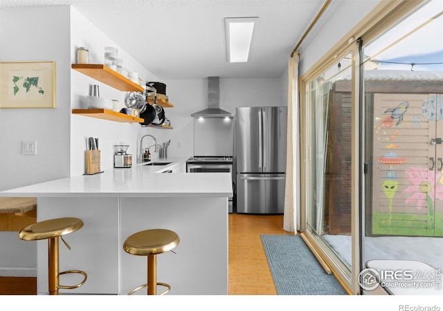 kitchen featuring sink, a kitchen bar, kitchen peninsula, stainless steel appliances, and wall chimney range hood