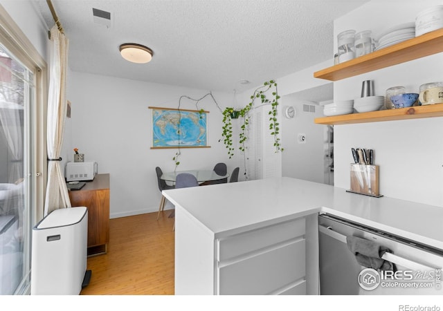 kitchen with dishwasher, a textured ceiling, kitchen peninsula, and light wood-type flooring