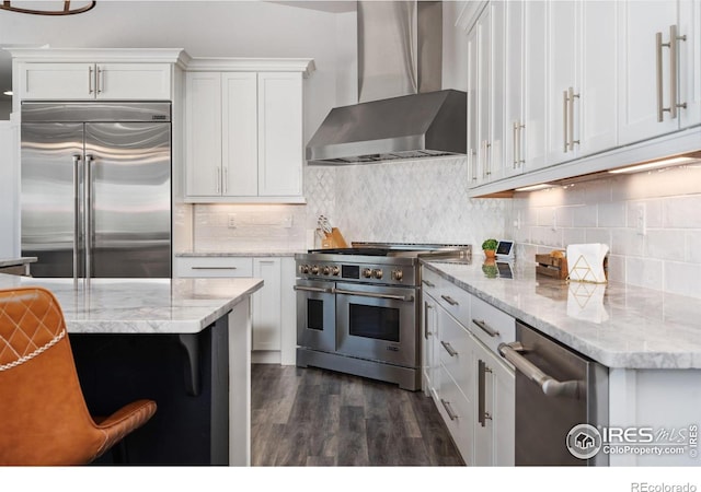 kitchen with white cabinetry, wall chimney range hood, backsplash, and high quality appliances