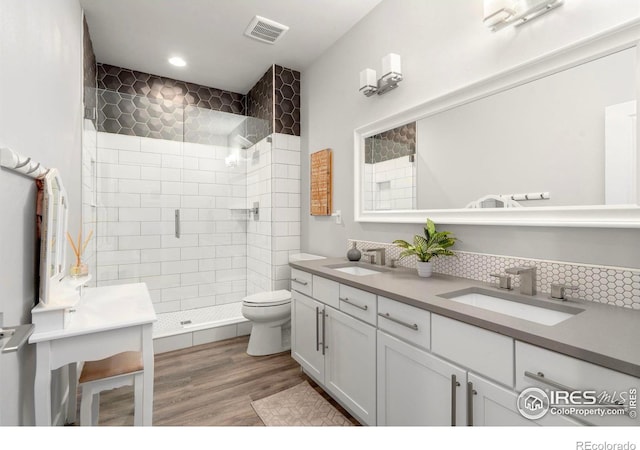 bathroom with hardwood / wood-style flooring, vanity, decorative backsplash, a shower with shower door, and toilet