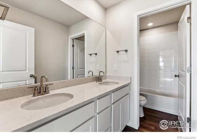 full bathroom featuring hardwood / wood-style flooring, vanity, tiled shower / bath combo, and toilet