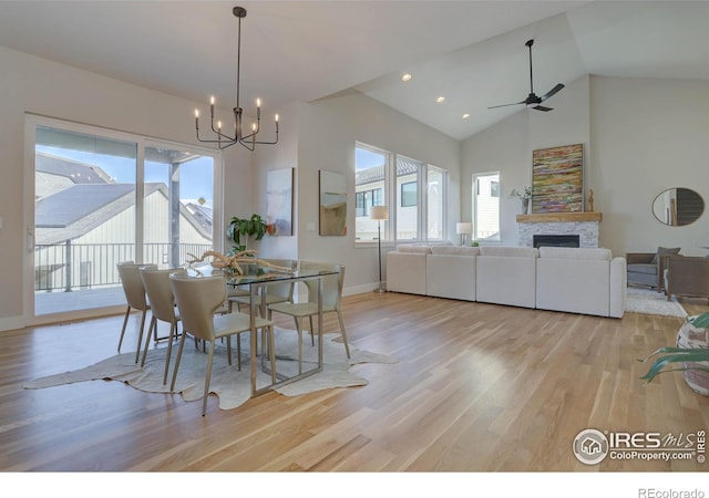 dining room with high vaulted ceiling, ceiling fan with notable chandelier, a fireplace, and light hardwood / wood-style floors