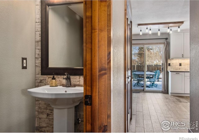 bathroom featuring hardwood / wood-style flooring, rail lighting, and decorative backsplash