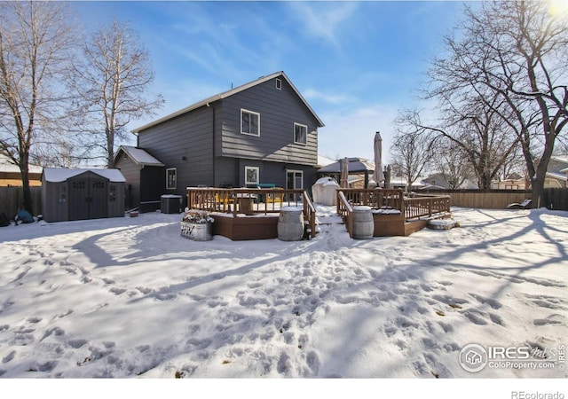 snow covered rear of property with a storage shed, a deck, and central air condition unit