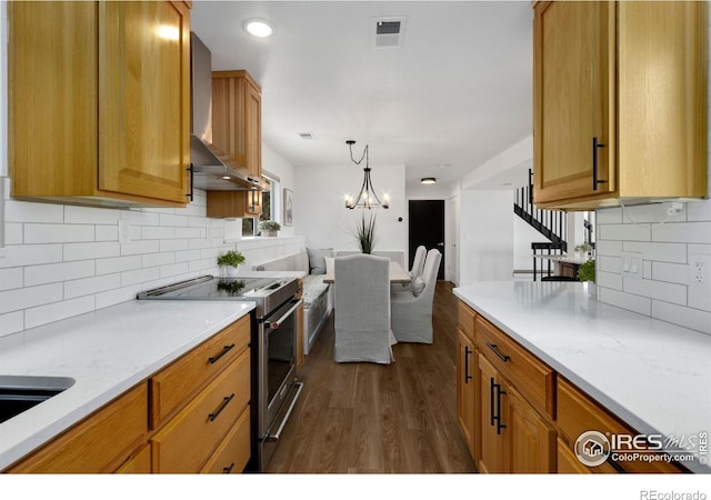 kitchen with dark hardwood / wood-style floors, stainless steel range with electric stovetop, light stone counters, wall chimney range hood, and an inviting chandelier