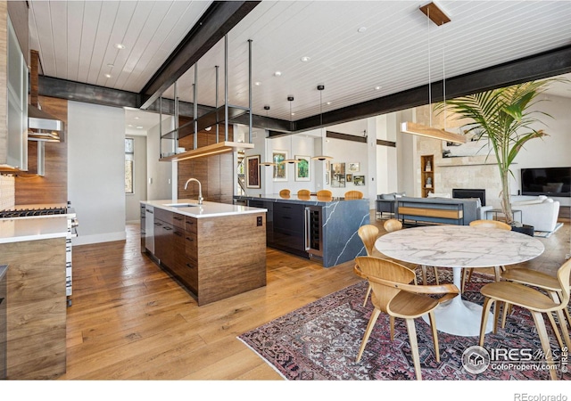 kitchen featuring sink, wood ceiling, light hardwood / wood-style flooring, an island with sink, and beamed ceiling