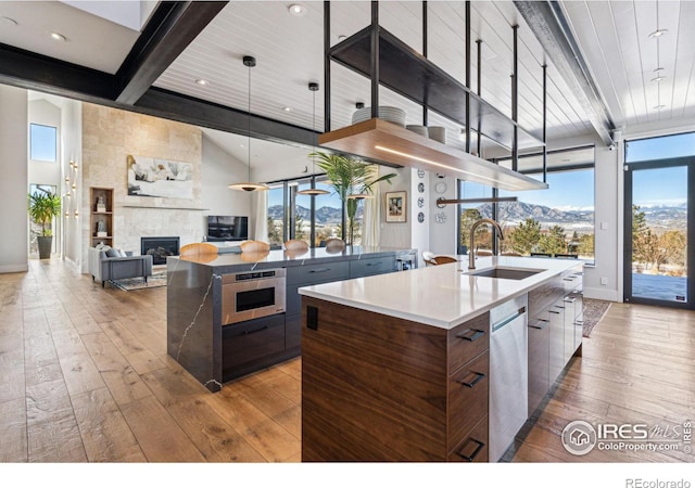 kitchen featuring sink, a mountain view, an island with sink, beamed ceiling, and light hardwood / wood-style floors