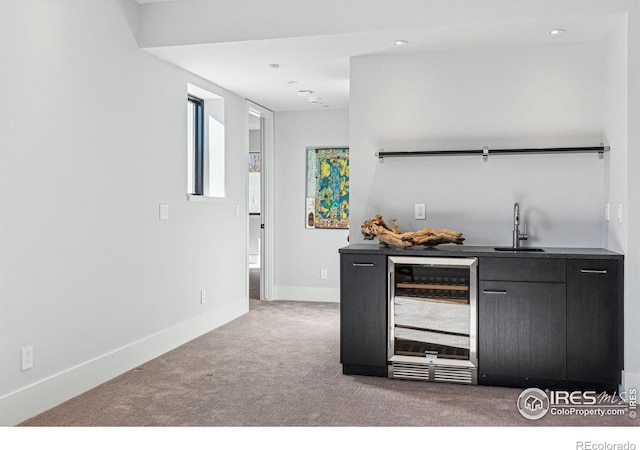 bar featuring beverage cooler, light carpet, a sink, baseboards, and wet bar