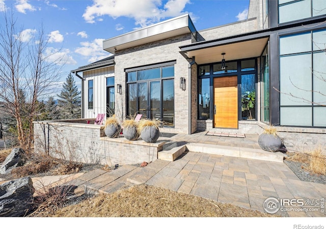 view of exterior entry with french doors, board and batten siding, and brick siding