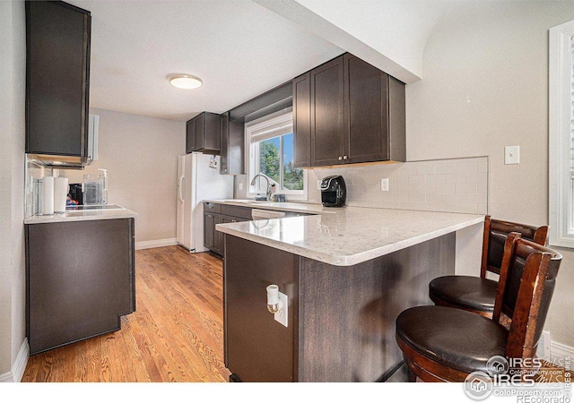 kitchen featuring a kitchen bar, kitchen peninsula, white refrigerator with ice dispenser, light hardwood / wood-style floors, and backsplash