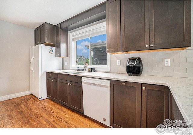 kitchen featuring tasteful backsplash, sink, dark brown cabinetry, light stone countertops, and white appliances