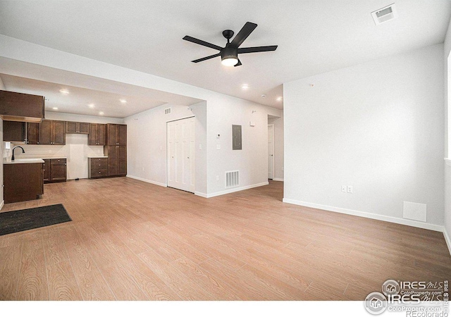 unfurnished living room with ceiling fan, sink, electric panel, and light hardwood / wood-style floors