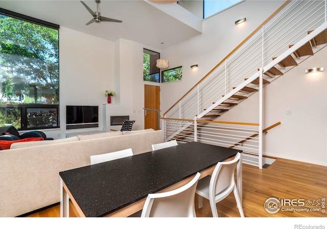 dining room featuring a towering ceiling, a wealth of natural light, ceiling fan, and hardwood / wood-style flooring