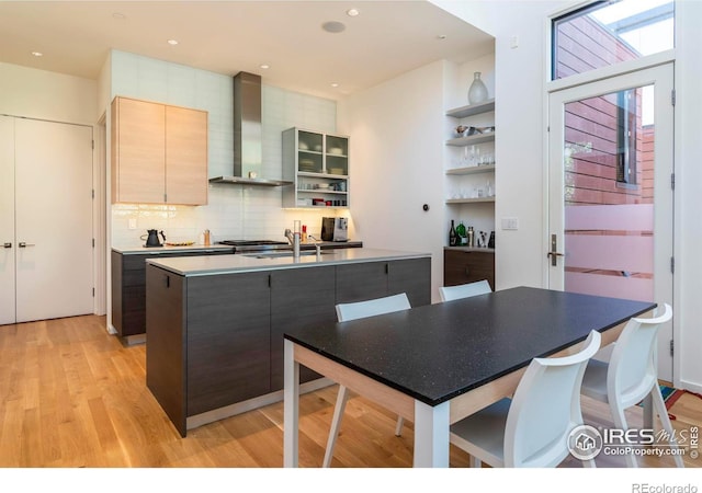 kitchen with sink, backsplash, light hardwood / wood-style floors, light brown cabinetry, and wall chimney exhaust hood