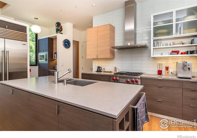 kitchen with tasteful backsplash, sink, a kitchen island with sink, range, and wall chimney exhaust hood