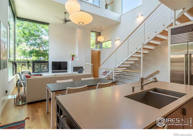 kitchen with built in fridge, a kitchen island, sink, a high ceiling, and light wood-type flooring