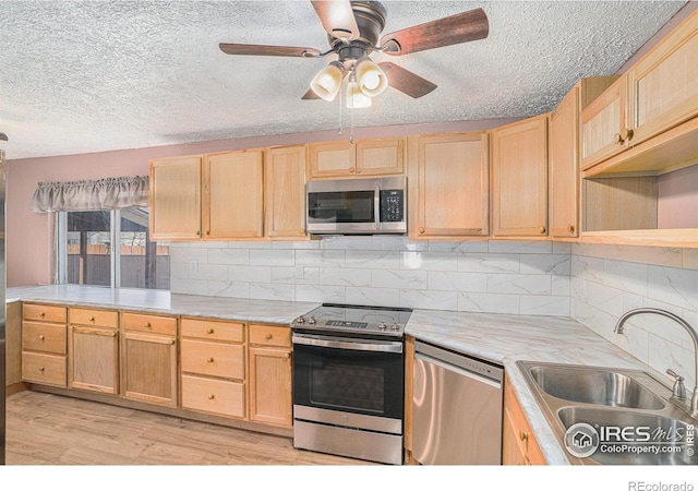 kitchen featuring appliances with stainless steel finishes, light brown cabinetry, tasteful backsplash, sink, and light hardwood / wood-style flooring