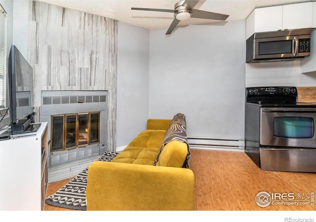 living room featuring light hardwood / wood-style flooring, a textured ceiling, baseboard heating, ceiling fan, and a tiled fireplace