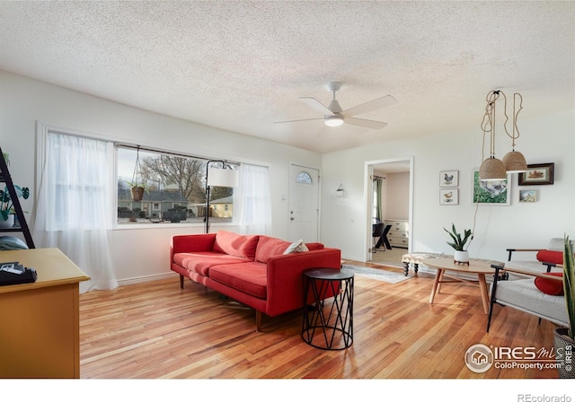 living room with light wood-style flooring, a ceiling fan, and a textured ceiling