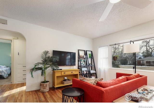 living room featuring arched walkways, a textured ceiling, wood finished floors, and a ceiling fan