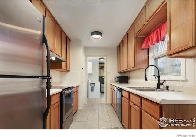 kitchen with brown cabinetry, under cabinet range hood, light countertops, black appliances, and a sink