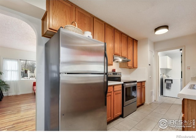 kitchen with brown cabinets, stainless steel appliances, light countertops, washer / dryer, and under cabinet range hood