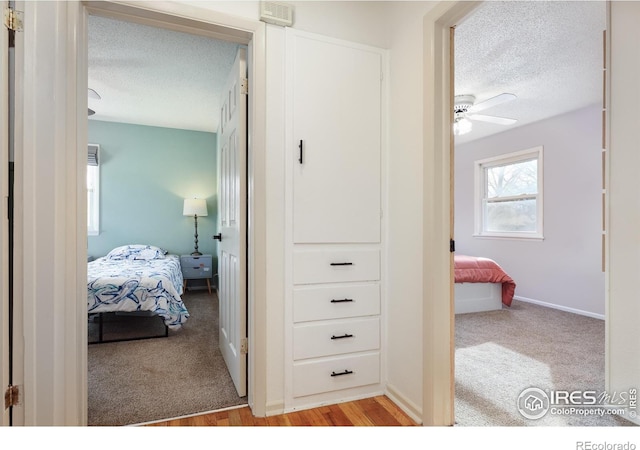 hallway featuring visible vents, light colored carpet, a textured ceiling, and light wood finished floors