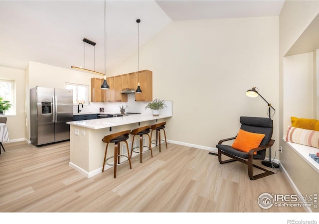 kitchen with a peninsula, a wealth of natural light, stainless steel refrigerator with ice dispenser, and under cabinet range hood