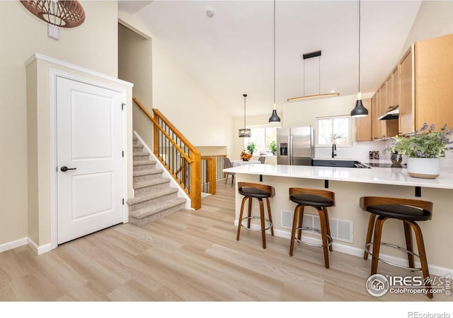 kitchen featuring visible vents, a peninsula, stainless steel refrigerator with ice dispenser, under cabinet range hood, and light wood-type flooring