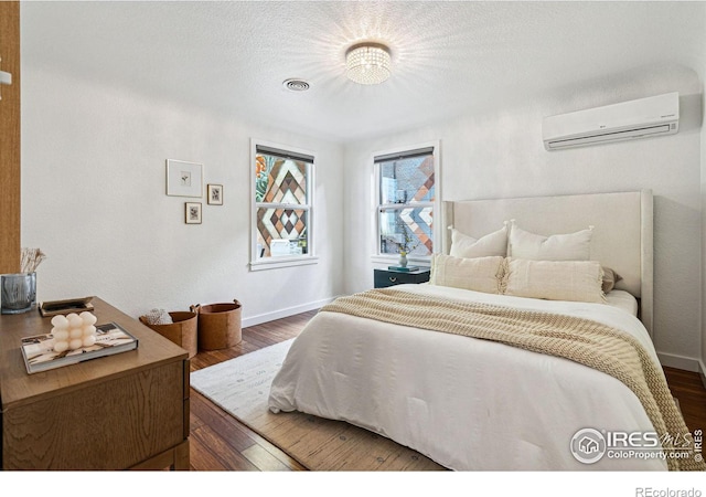 bedroom featuring dark hardwood / wood-style flooring, a wall mounted air conditioner, and a textured ceiling