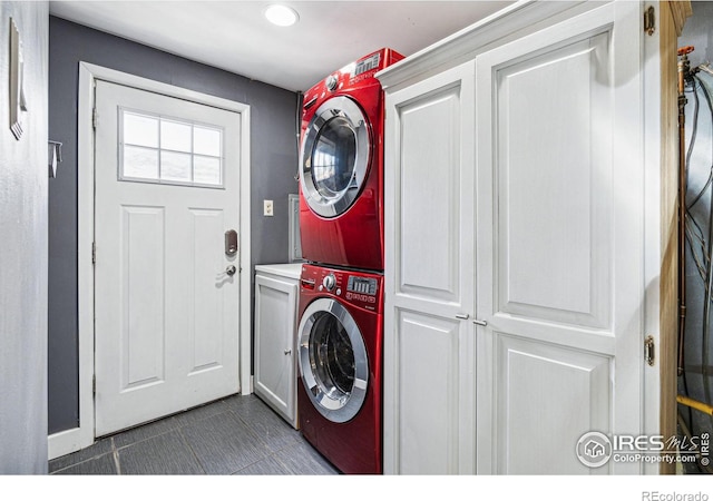 washroom featuring stacked washer and dryer, cabinets, and dark tile patterned flooring