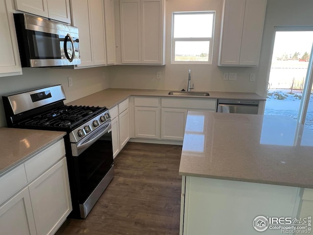 kitchen with sink, appliances with stainless steel finishes, plenty of natural light, light stone countertops, and white cabinets