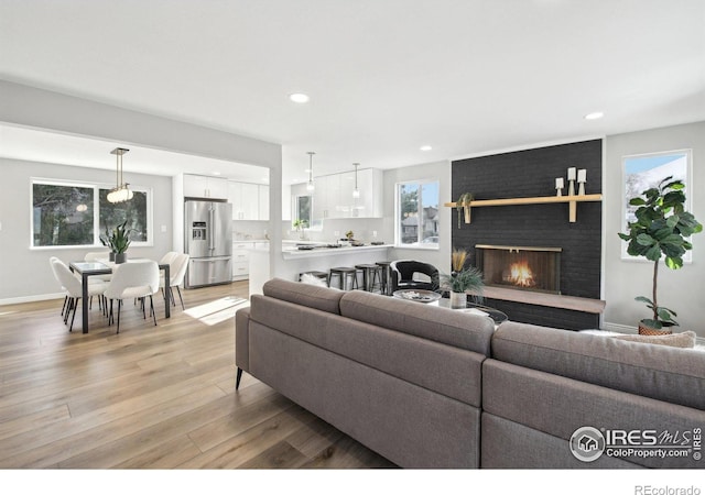 living area featuring light wood finished floors, a brick fireplace, baseboards, and recessed lighting