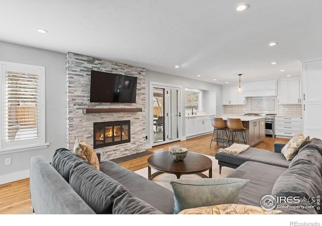 living room with sink, a stone fireplace, plenty of natural light, and light hardwood / wood-style floors