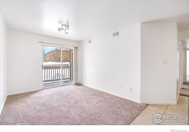 spare room with a textured ceiling, visible vents, baseboards, tile patterned floors, and carpet