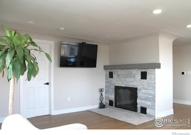 living room featuring a stone fireplace and dark wood-type flooring