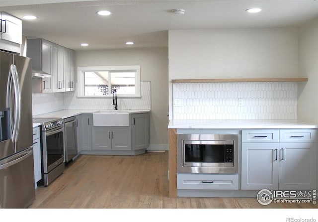 kitchen with sink, gray cabinets, light hardwood / wood-style flooring, stainless steel appliances, and tasteful backsplash