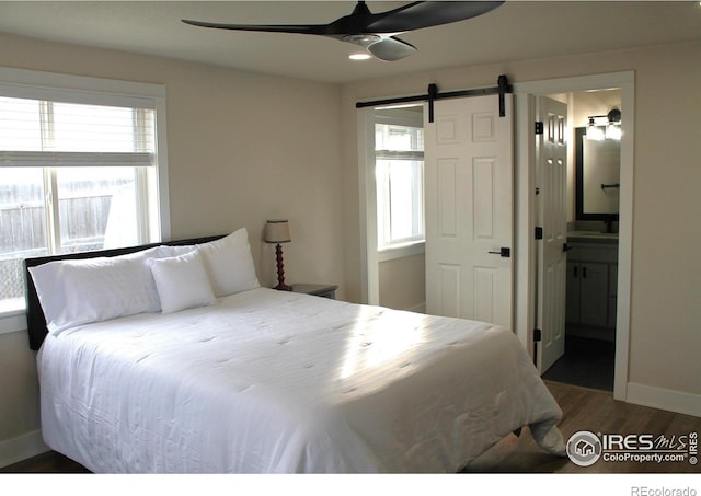 bedroom featuring multiple windows, connected bathroom, dark hardwood / wood-style flooring, and a barn door