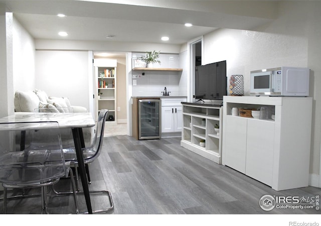 kitchen with wine cooler, hardwood / wood-style floors, decorative backsplash, and white cabinets