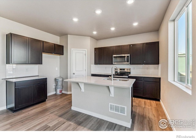 kitchen with an island with sink, appliances with stainless steel finishes, sink, and dark brown cabinetry